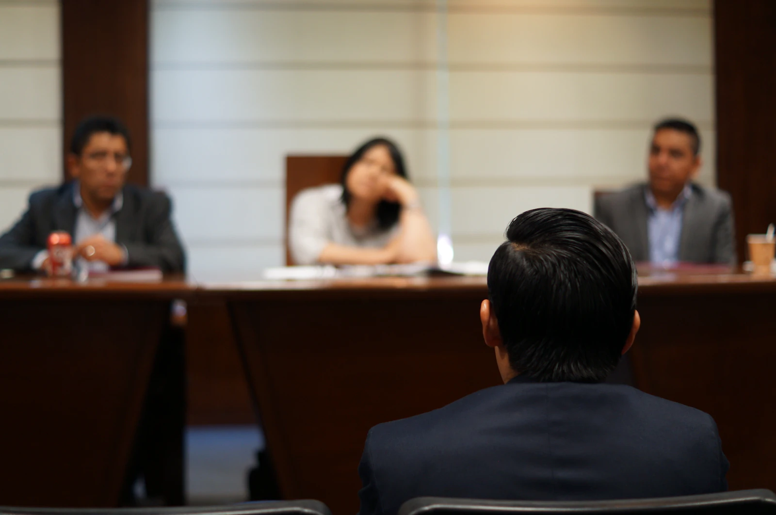 An attorney standing to address people seated at a long wooden table in a hearing room.