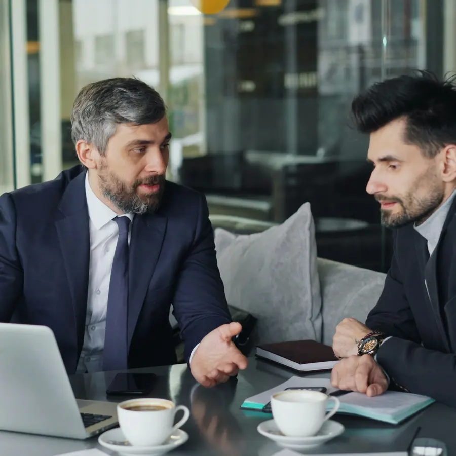 Two attorneys in suits reviewing a case file together across a table in an office.